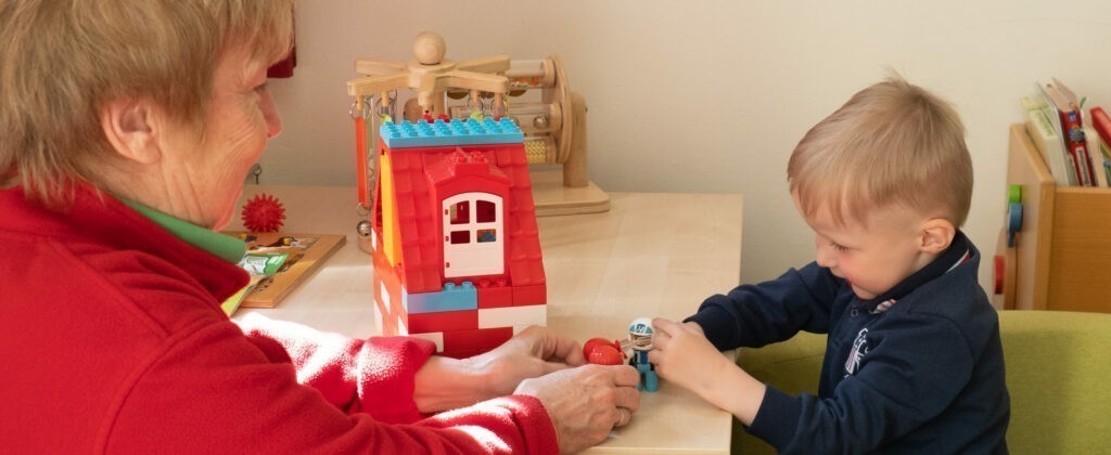 Eine ältere Frau spielt mit einem kleinen Jungen auf einem Tisch mit Duplo-Lego