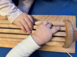 Zwei Babyhände tasten an einem Holzspielzeug